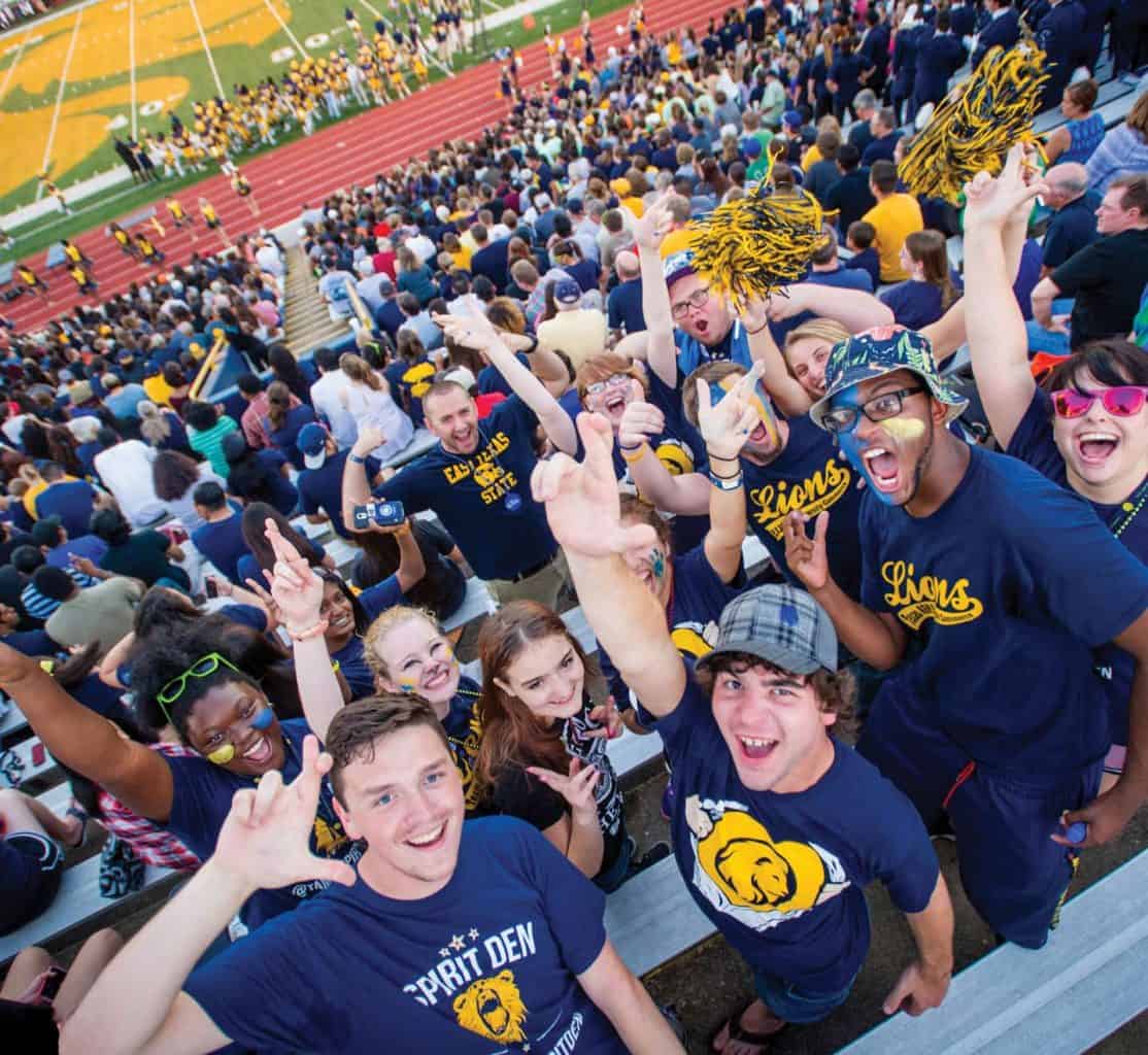 a group of students signing the leo sign at a football game. 