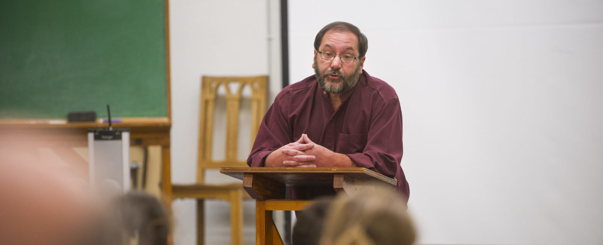 Man reading to a classroom from a podium.