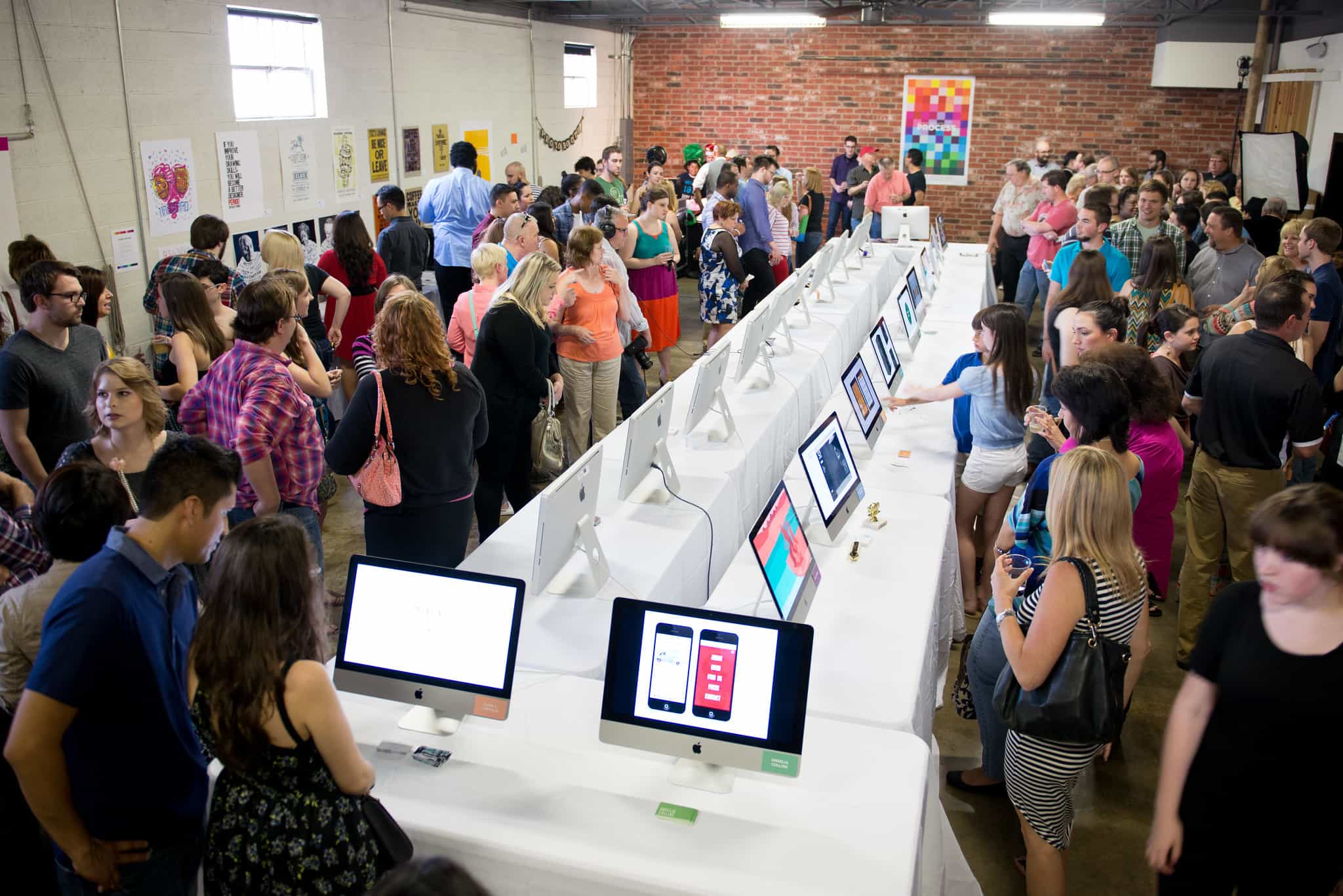 Large group surrounding tables of computers exhibiting design work.