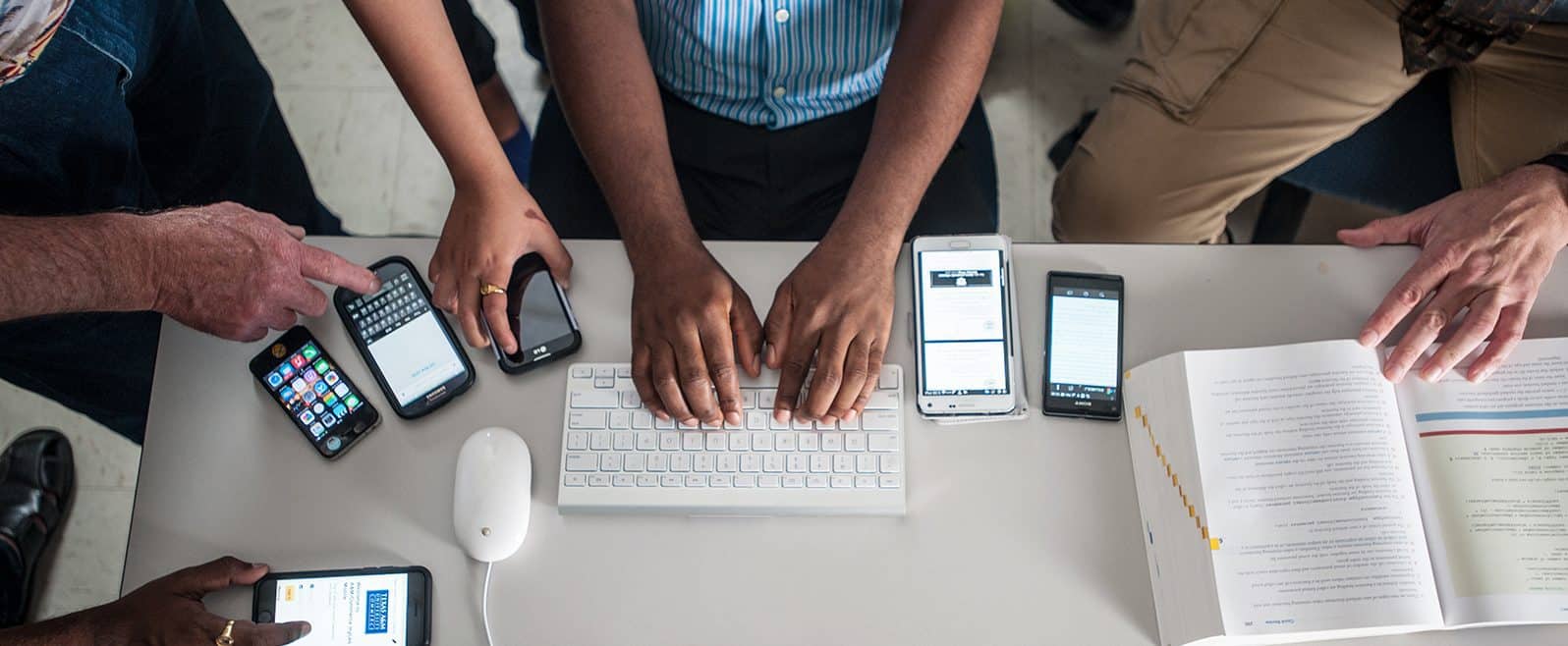 Students working at desk with cell phones, keyboard and textbook