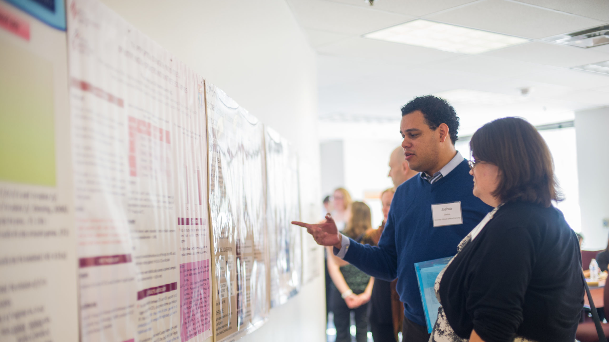 Two professionals looking and discussing material hanging on walls during a linguistics second language conference.