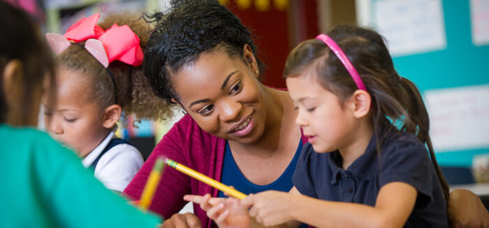 Female teacher with elementary age girl at school desk.