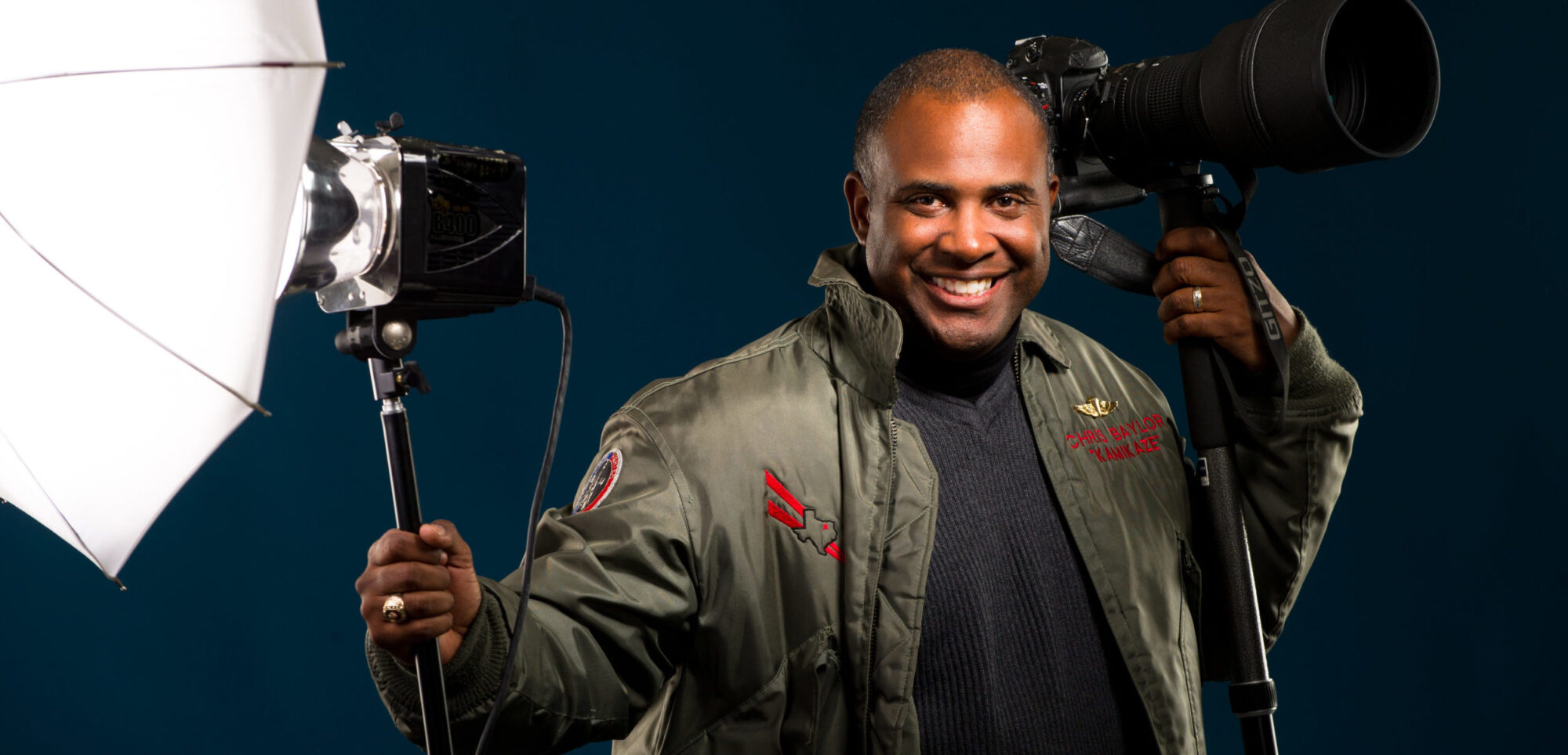 Black male photographer with with camera and strobe in hand.