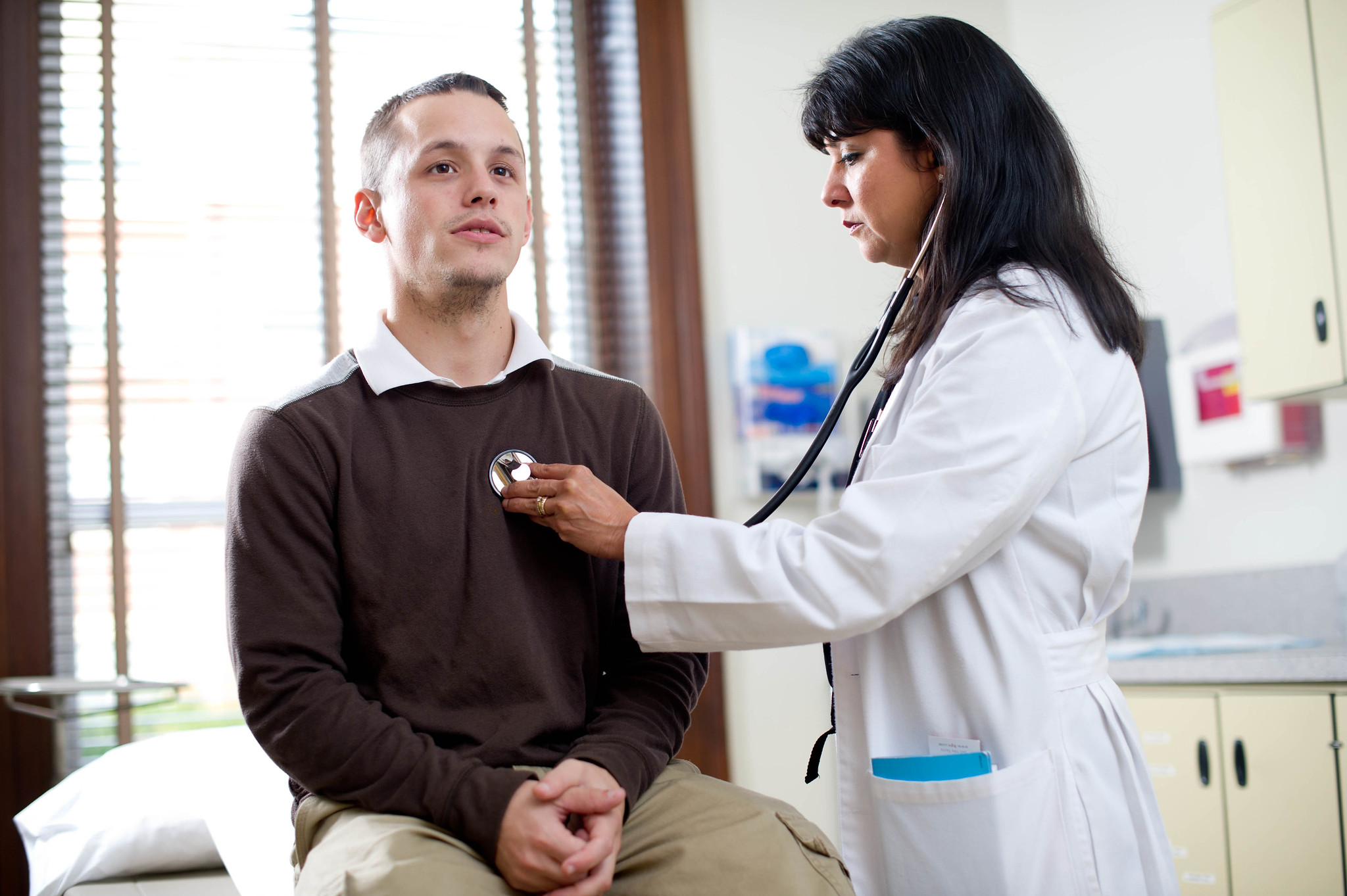 Nurse listening to male patient's heart.