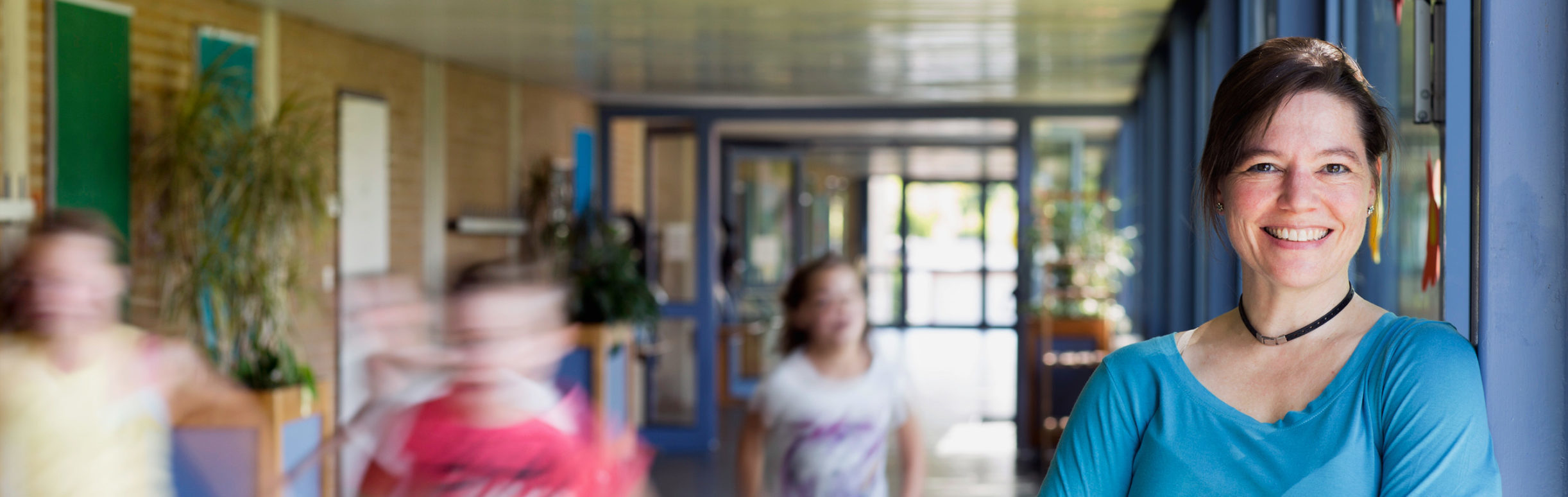 Woman standing in a school hallway with children running by.