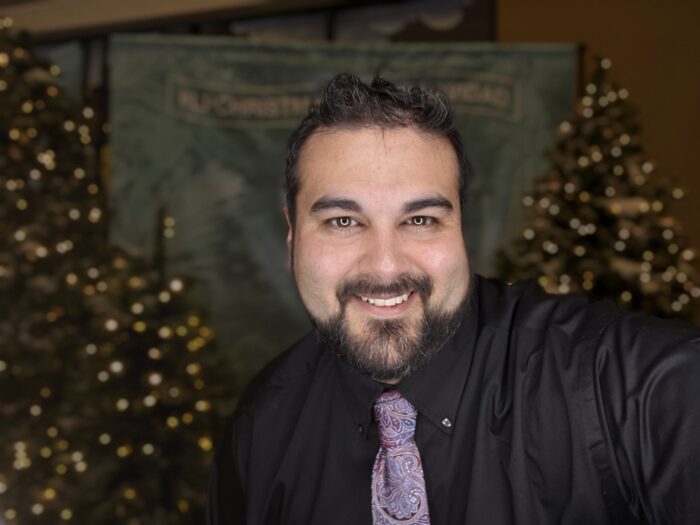 Jeremy Gamez smiling at the camera with Christmas trees behind him.