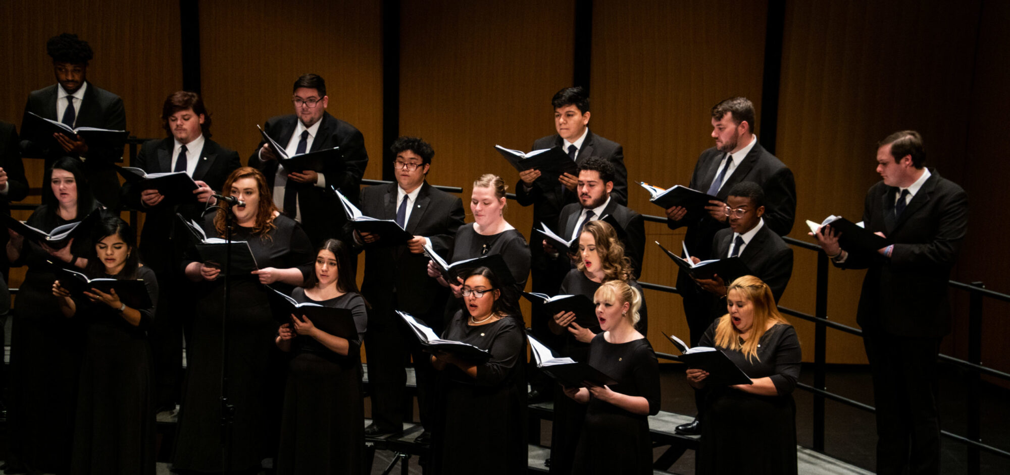 Choir performing on stage wearing formal attire.