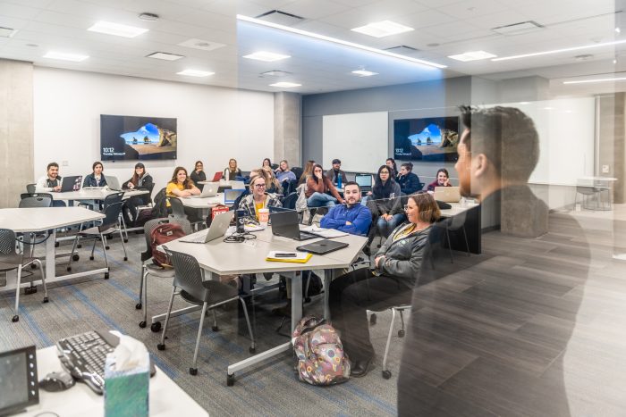 a photo of students in a classroom taken from outside of a glass wall.