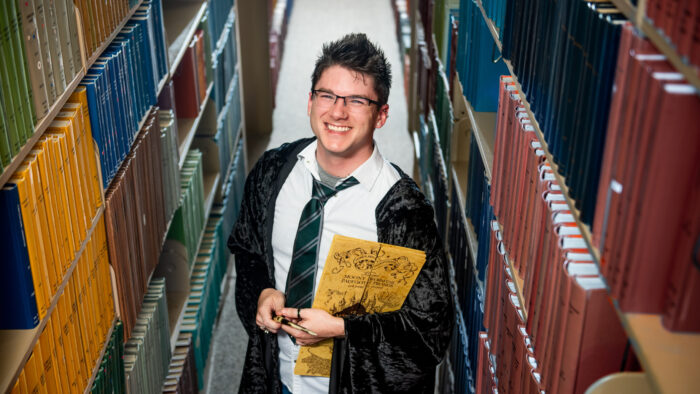 An instructor in wizard apparel stands between isles of books