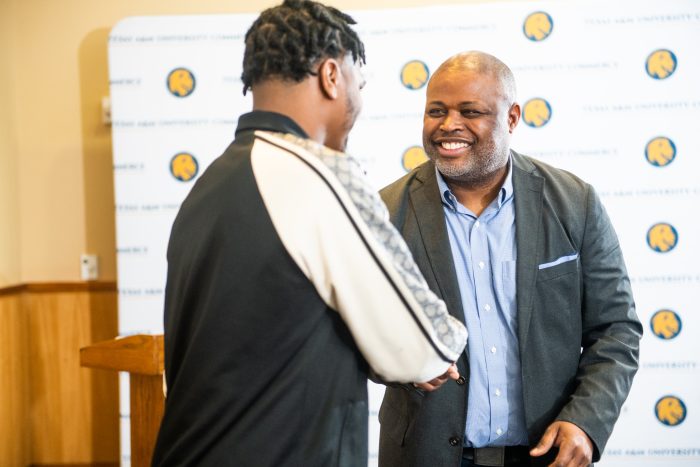 One male student shaking hands with male professor.