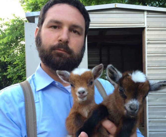 Paul Bryan with two goat kids background goat shed