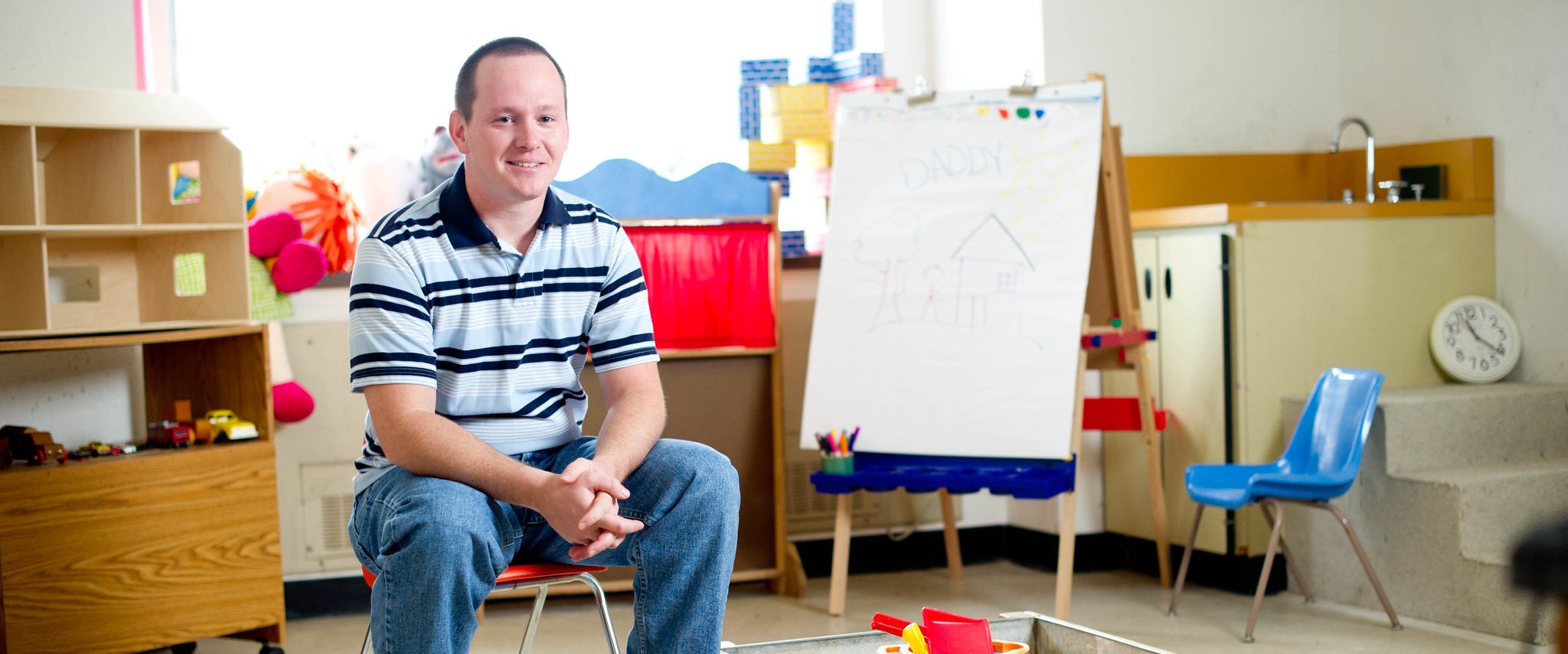 Man sitting by a sandbox in a classroom.