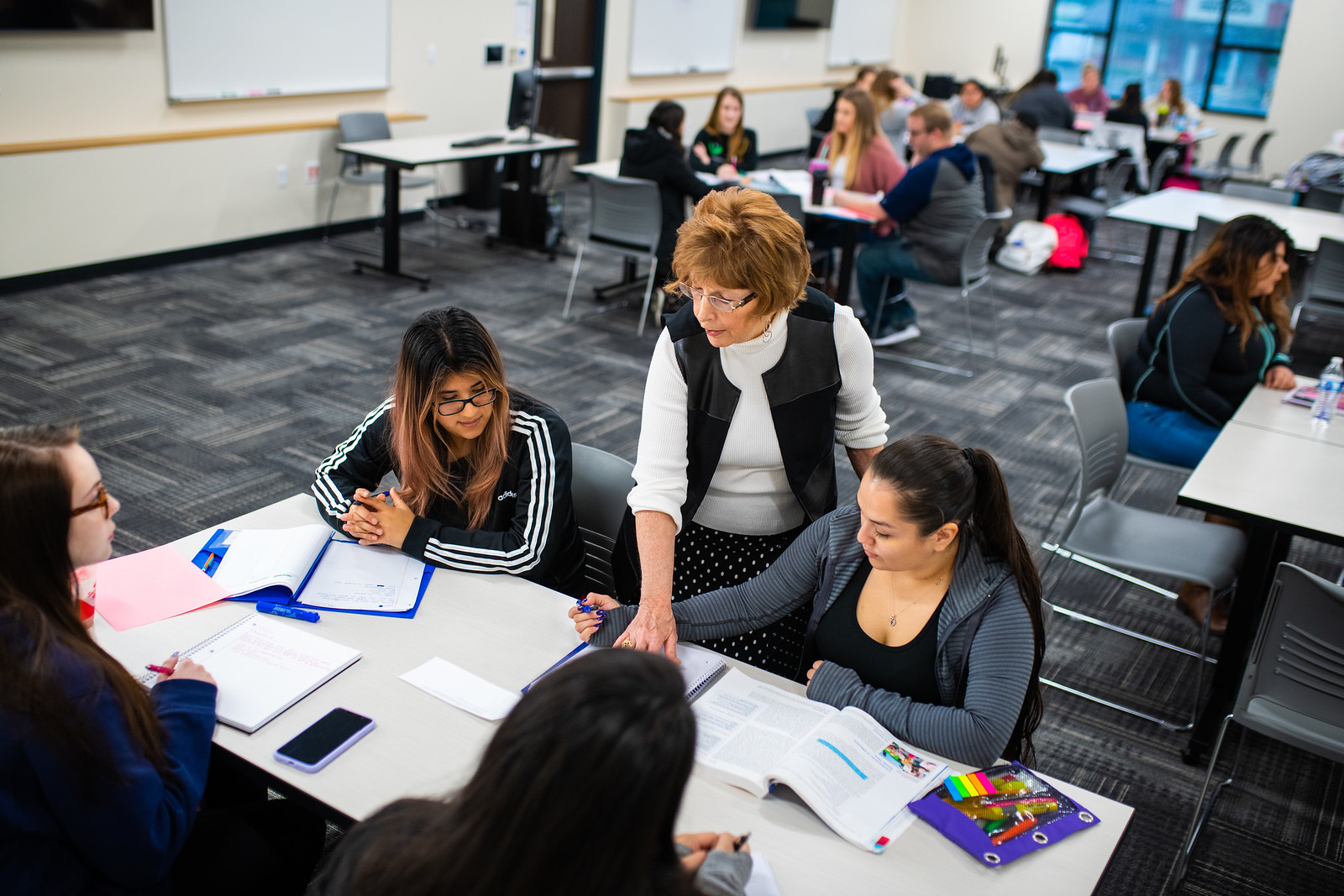 Female instructor working with two young women at a classroom desk.