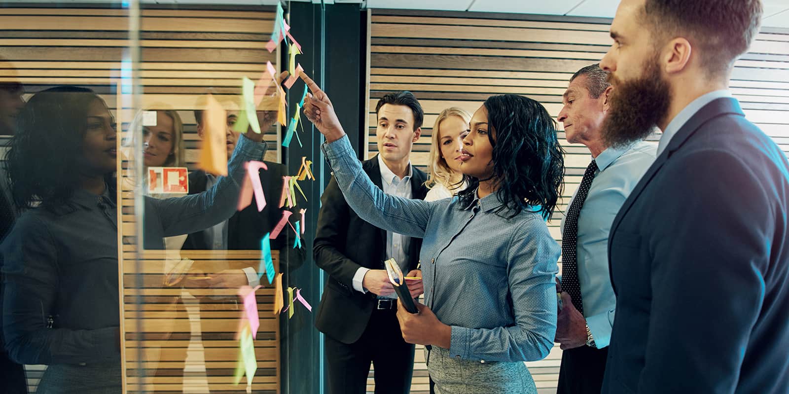 Creative group of business people brainstorming putting sticky notes on glass wall in office.