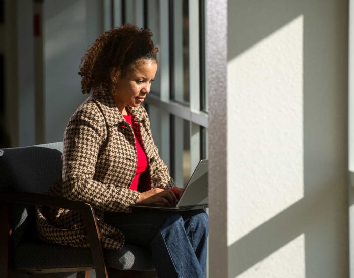 Woman working on a computer sitting by windows.