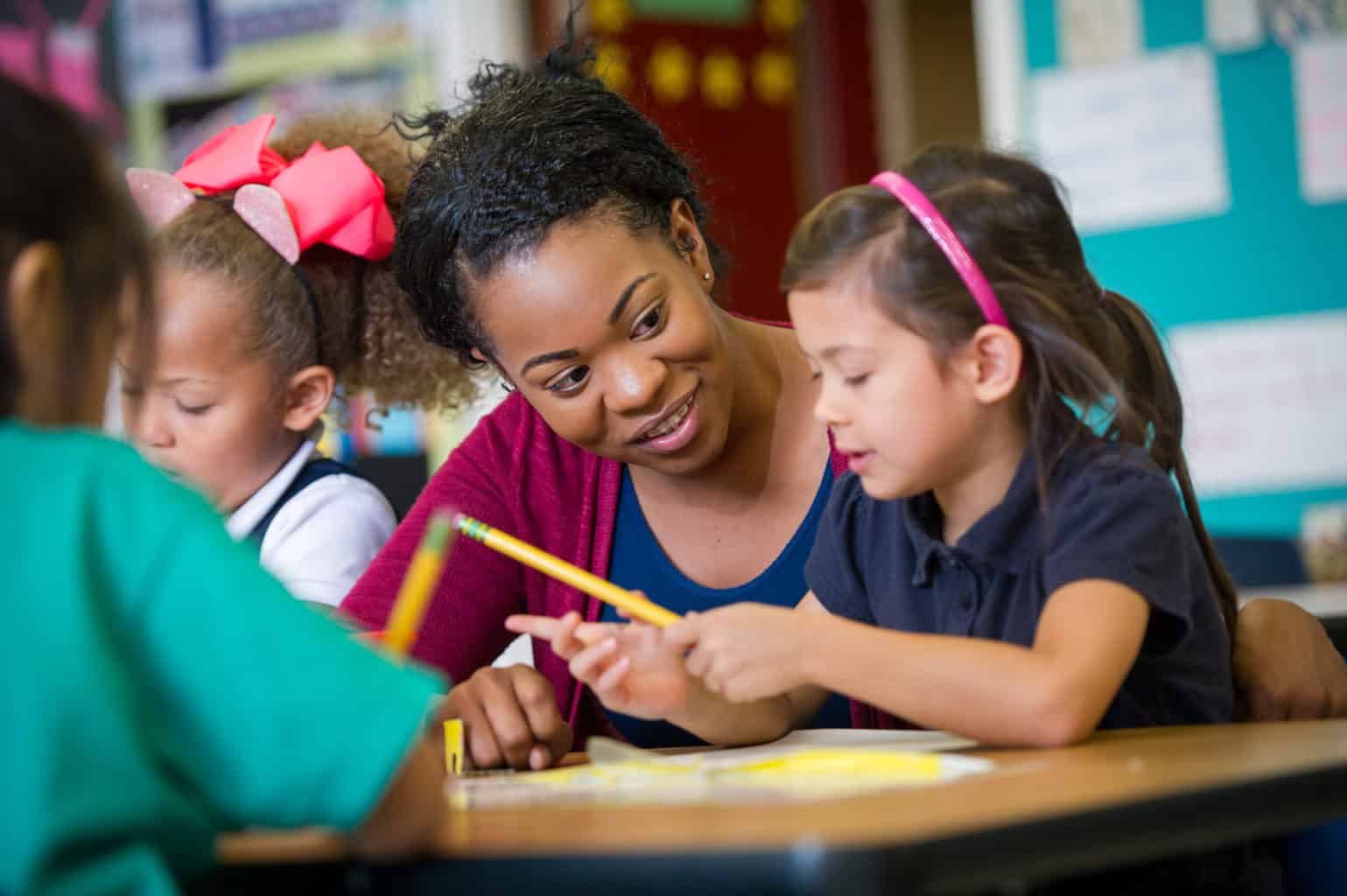 Female teacher with elementary age girl at school desk.