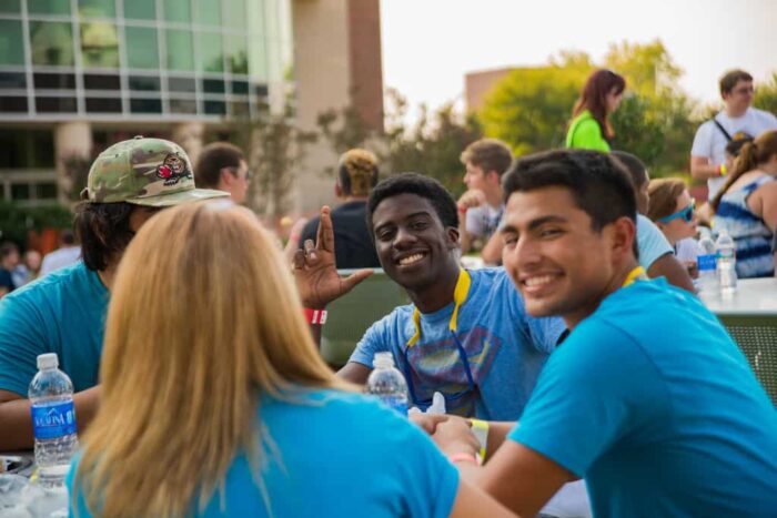 Group of students siting at table outside smiling at the camera.