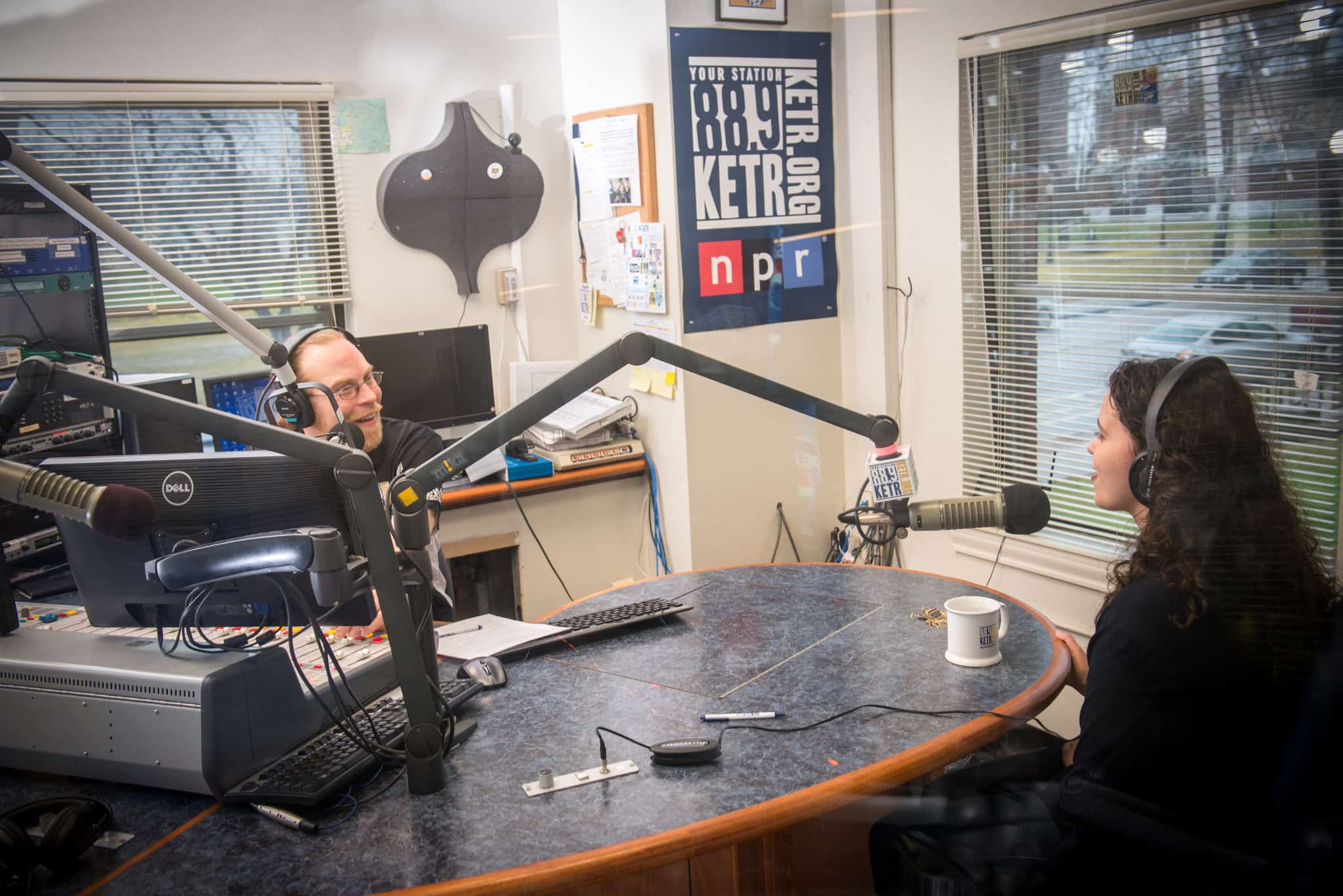 A man is speaking to a young female at the KETR radio studio.