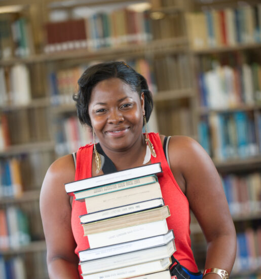 Woman in library holding a stack of books.