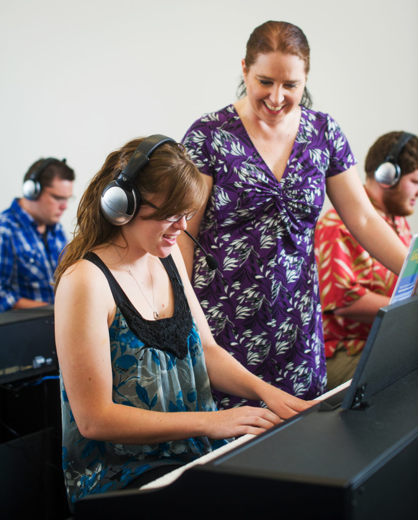 student playing keyboard with instructor observing with smile.