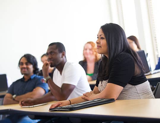 Students in class sitting down at desks listening to lecture.