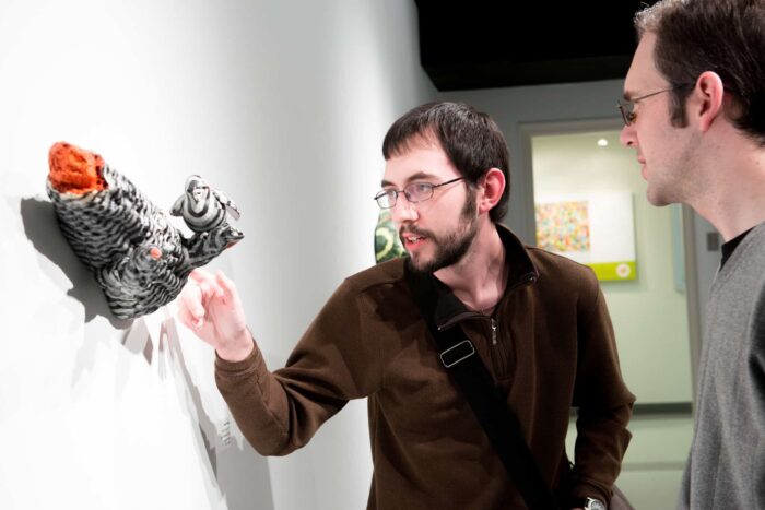 Two men reviewing 3 dimensional art piece hanging on wall.