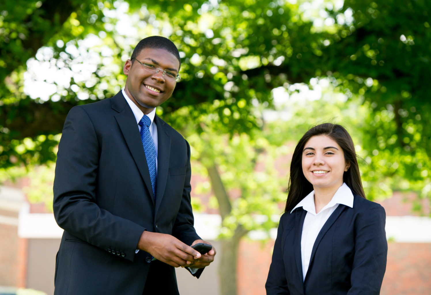 Two students dressed professionally standing outside on campus.