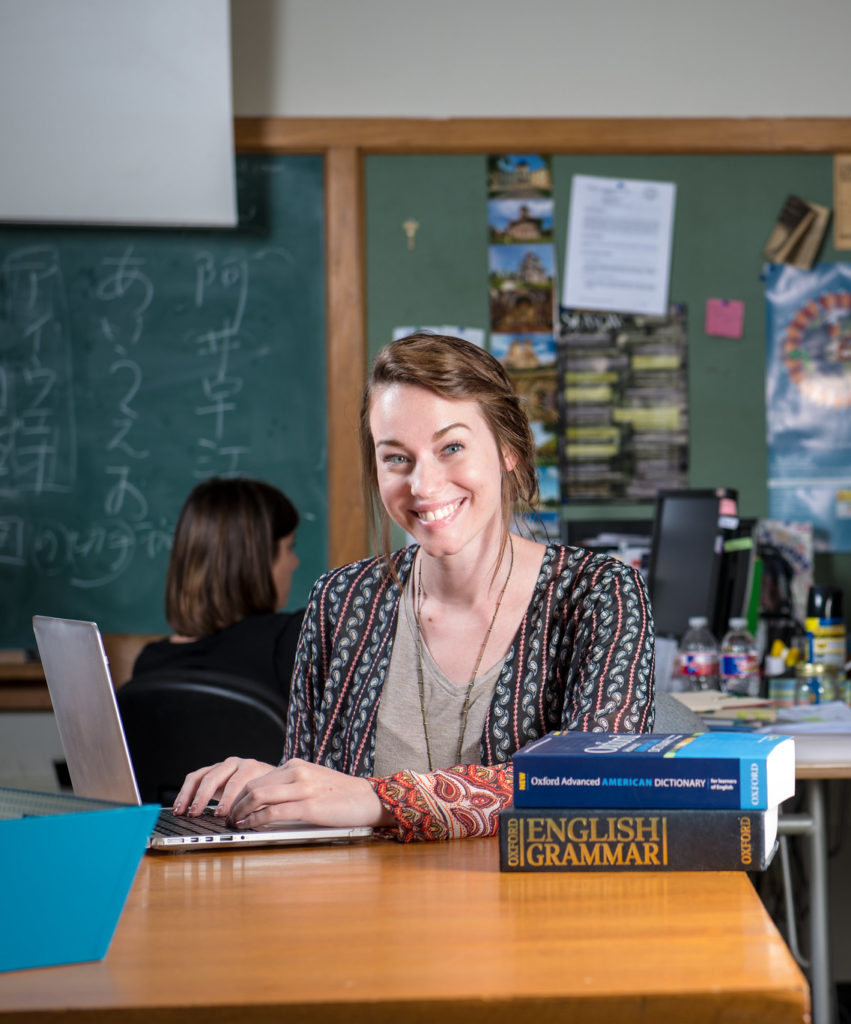 Girl in classroom with textbooks and a laptop.