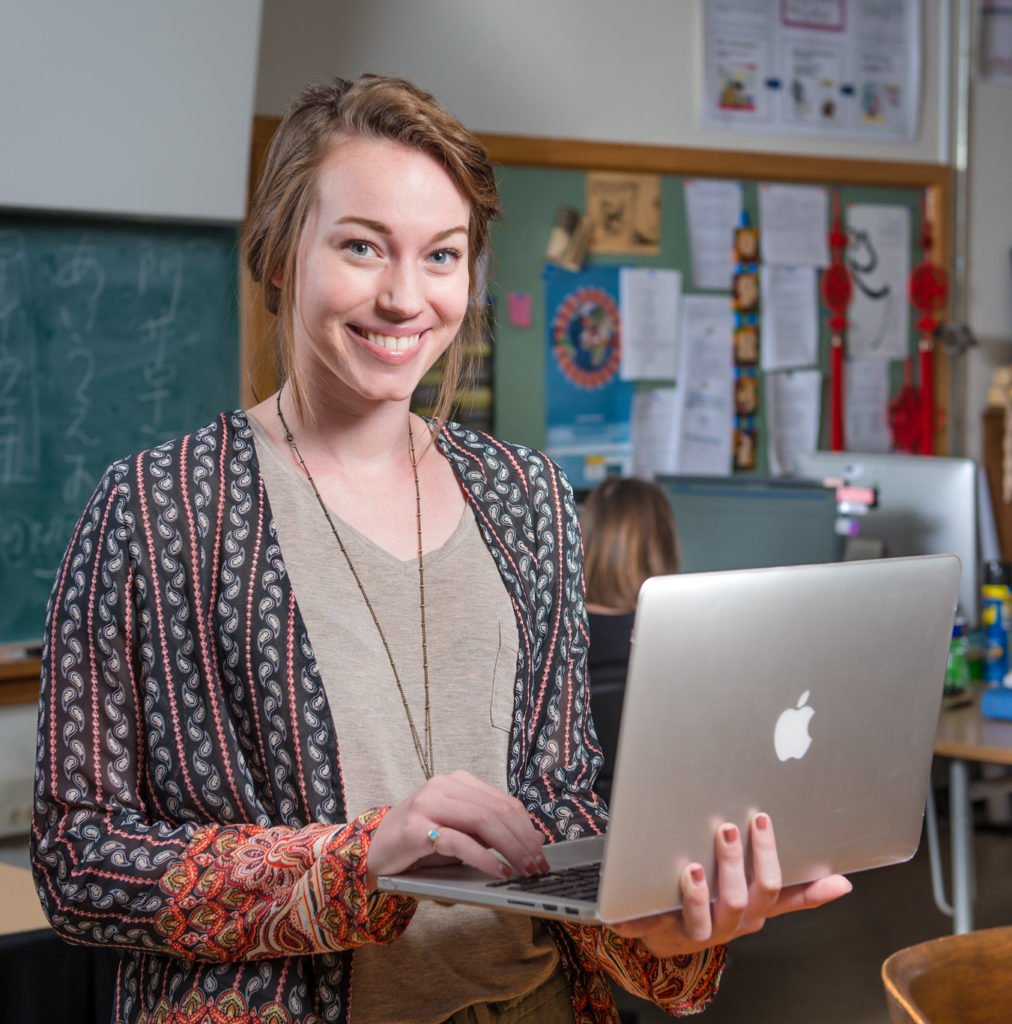 Woman standing in classroom with a laptop.