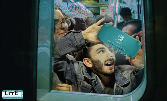 Young adult squished into a subway train, but still enjoying their handheld video game system.