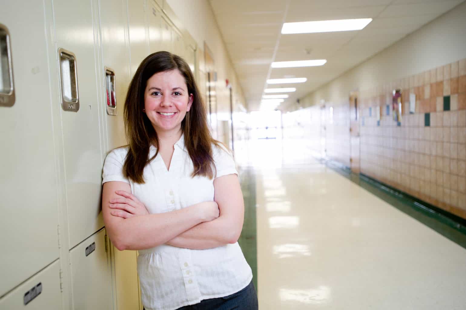 Woman school counselor standing in front of lockers.