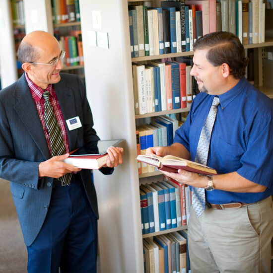 Two male professor in the library taking with books in their hands.