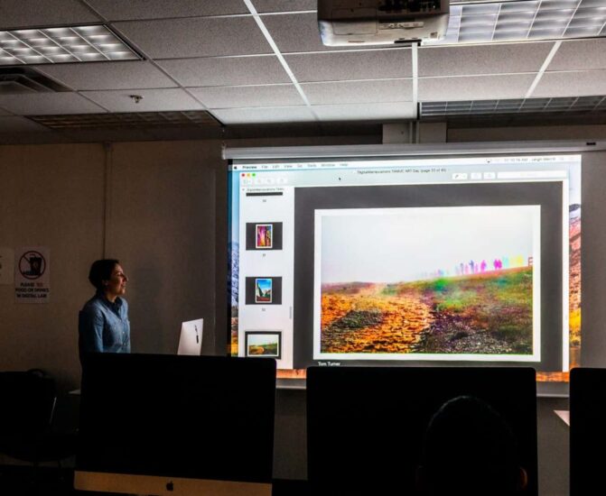 Instructor teaching course in dark class with projector.