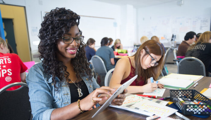 Young African American woman working on tablet in a classroom of college students.