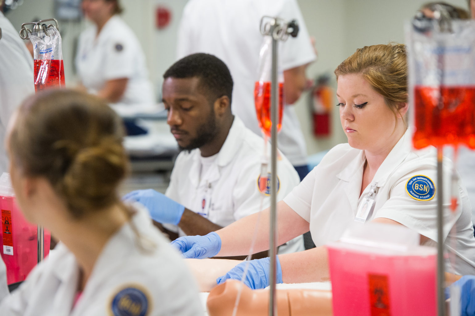 Nurses in classroom with gloves and practicing setting IVs