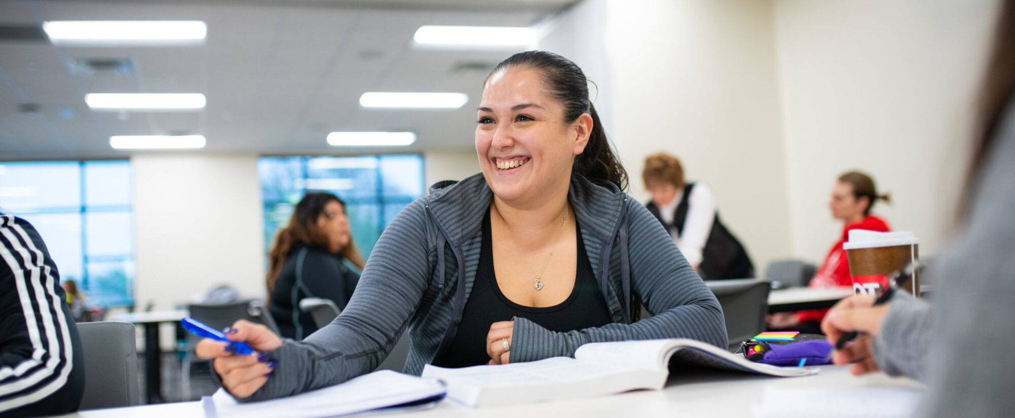 Woman smiling with pen and books in front of her.