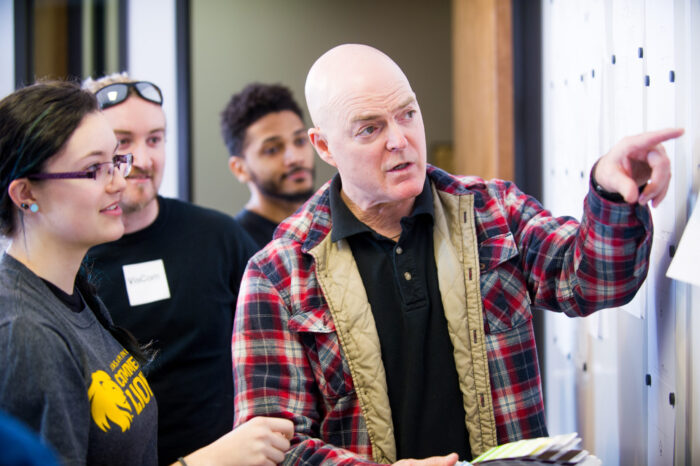 VisCom faculty member speaking to group while pointing at a display board.