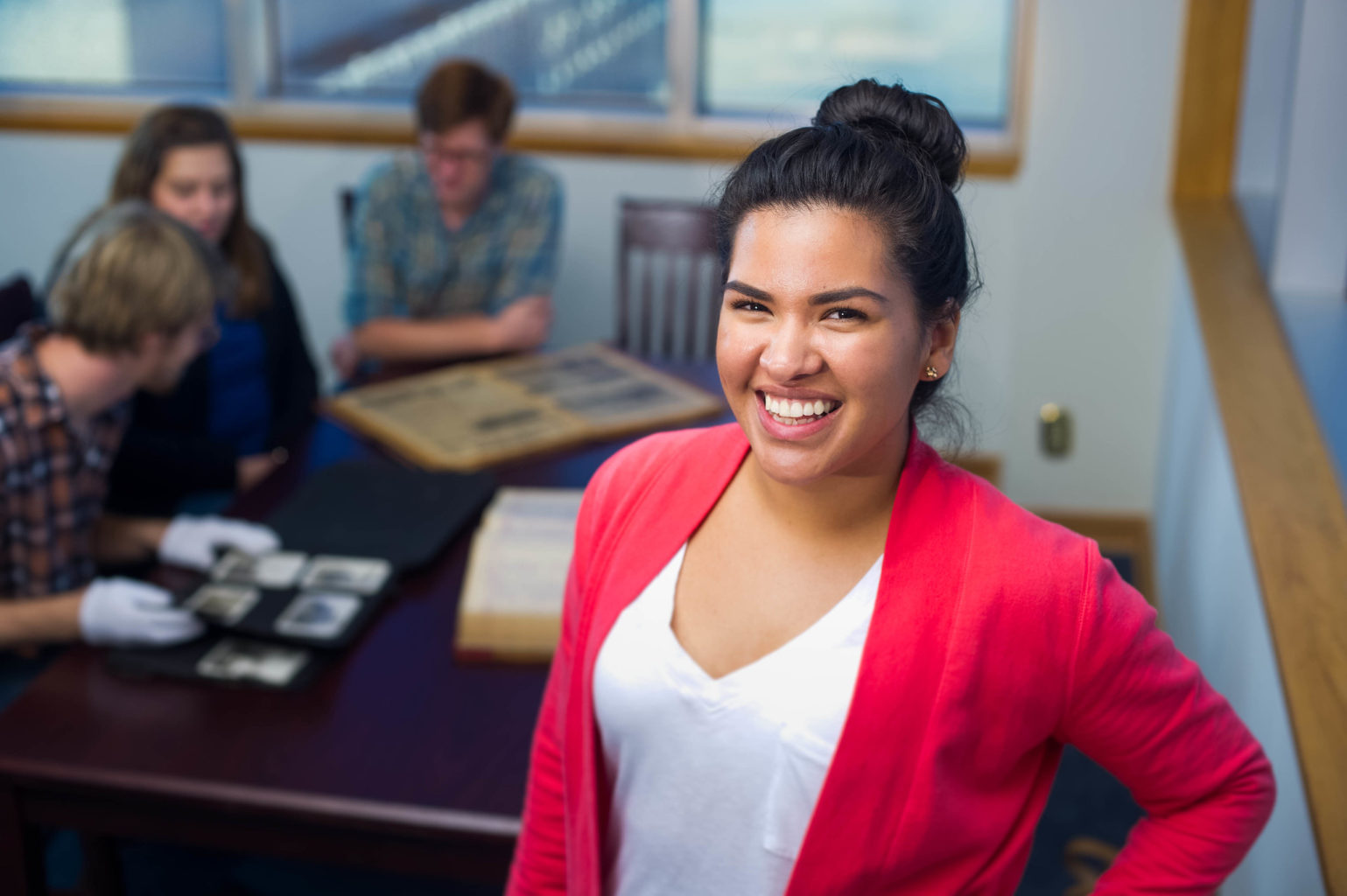 Young woman smiling with students looking at historic photographs in the background.