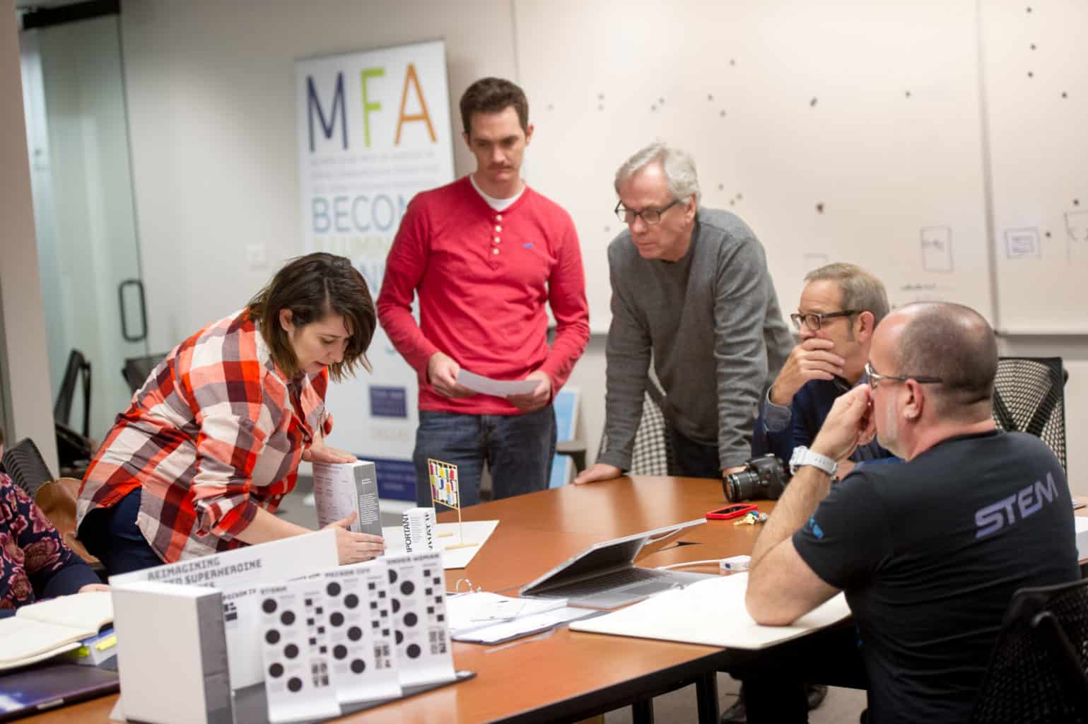 5 students surrounding table in VisComm MFA classroom.