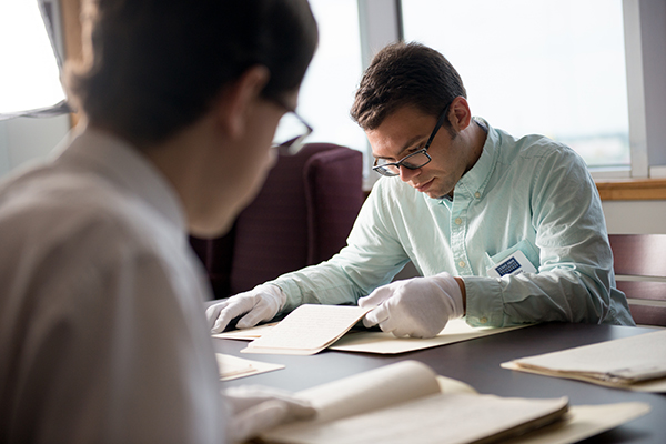 Two students looking over historical documents using gloves.