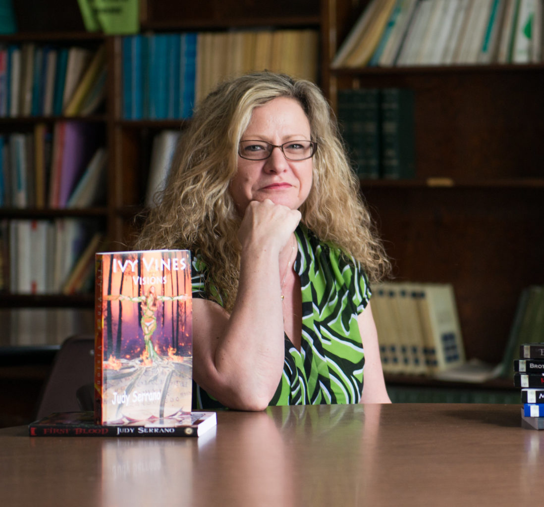 English professor sitting with books in the library.