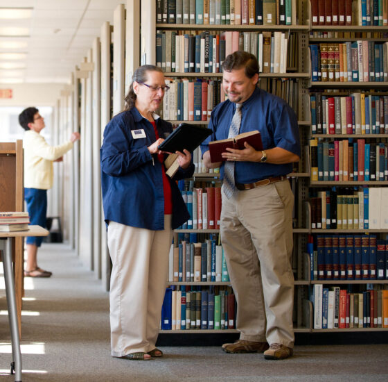 Two people examining books in a library.