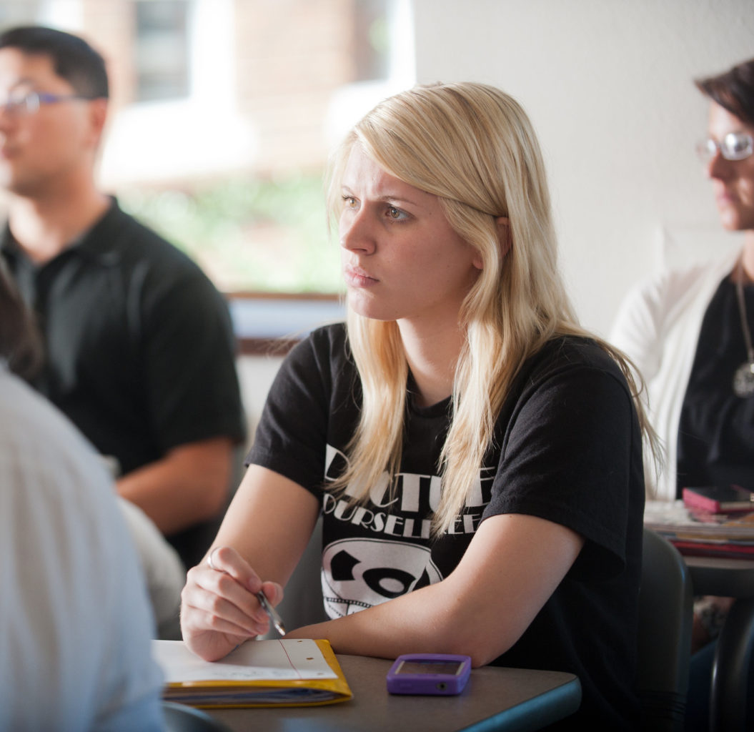 Young woman in classroom with pen and paper.