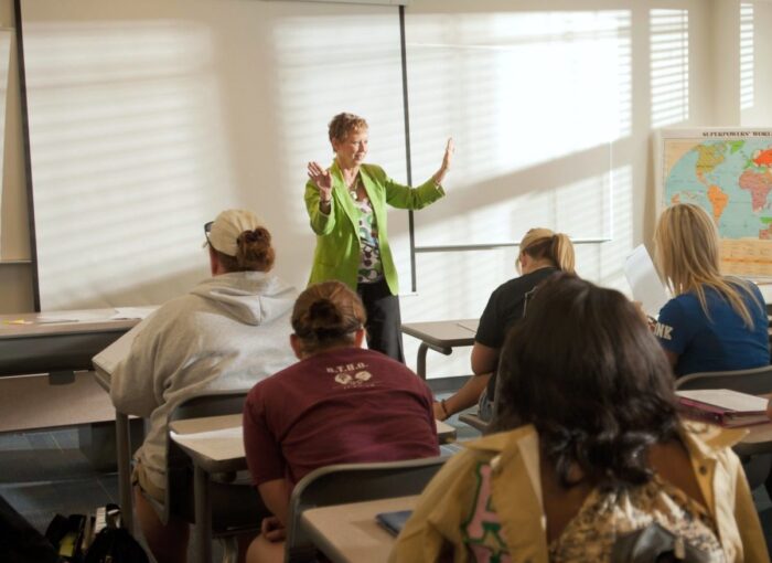 Female teacher instructing college students in classroom.