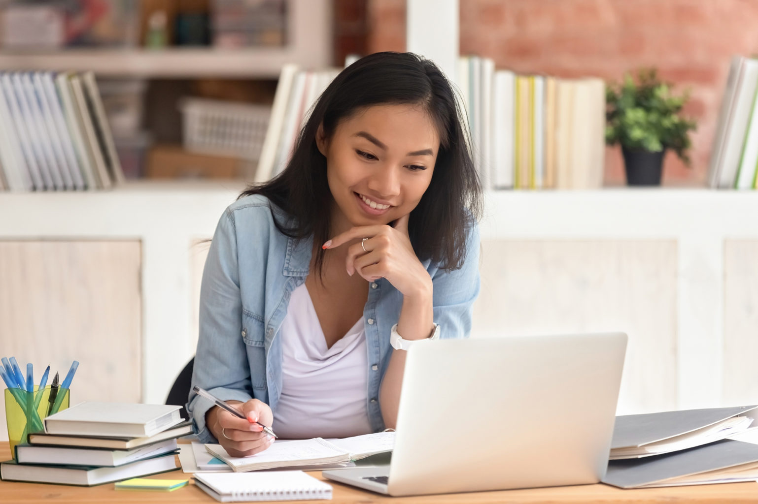 A applied criminology student sitting down at a desk, taking notes and looking at the screen of a laptop.