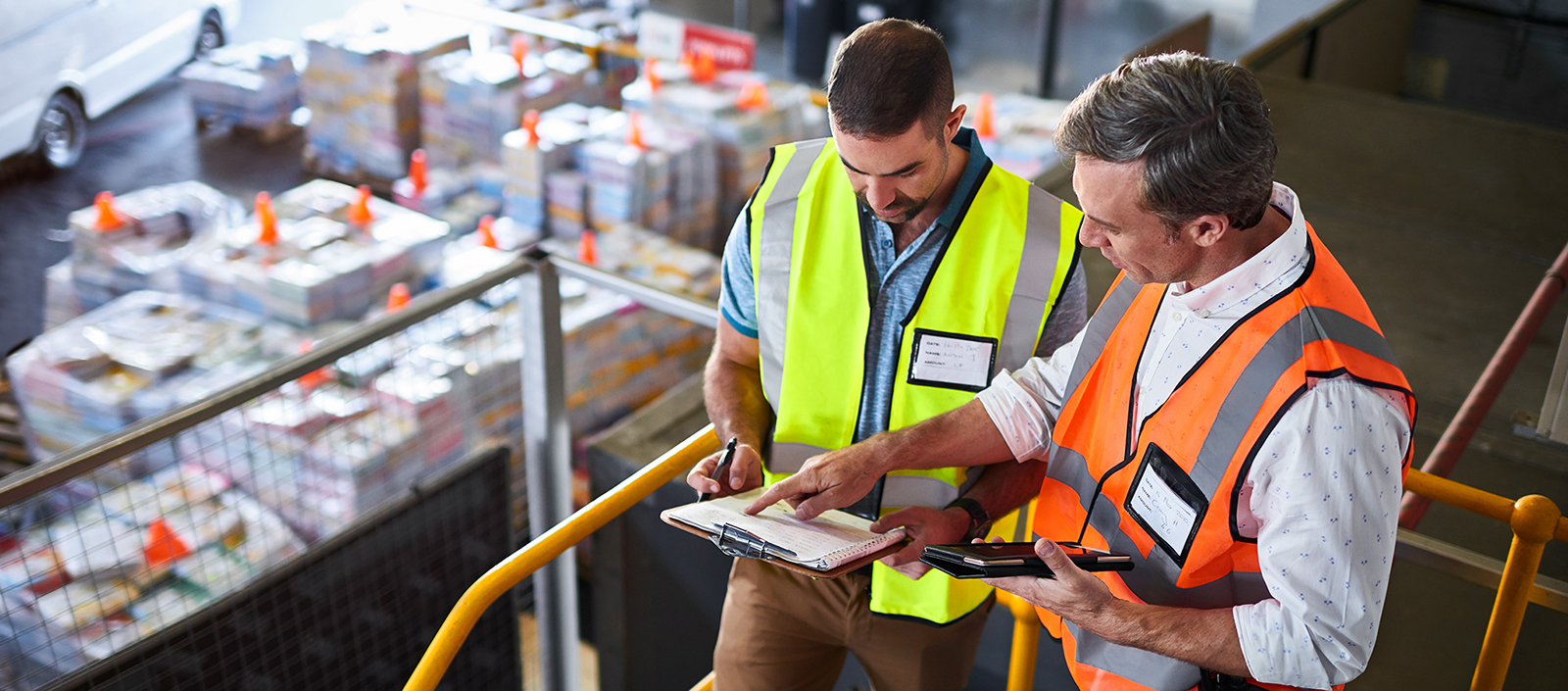 Shot of two warehouse workers standing on stairs using a digital tablet and looking at paperwork.