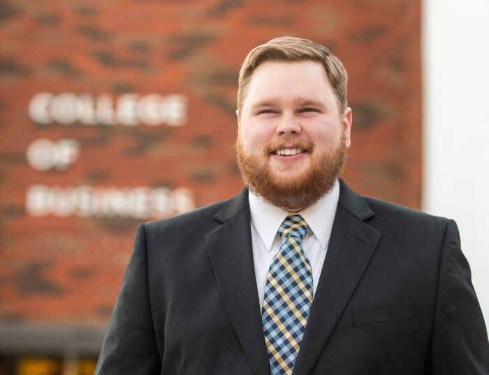 A gentlman by the name Chase Miller standing in front of the College of Business.