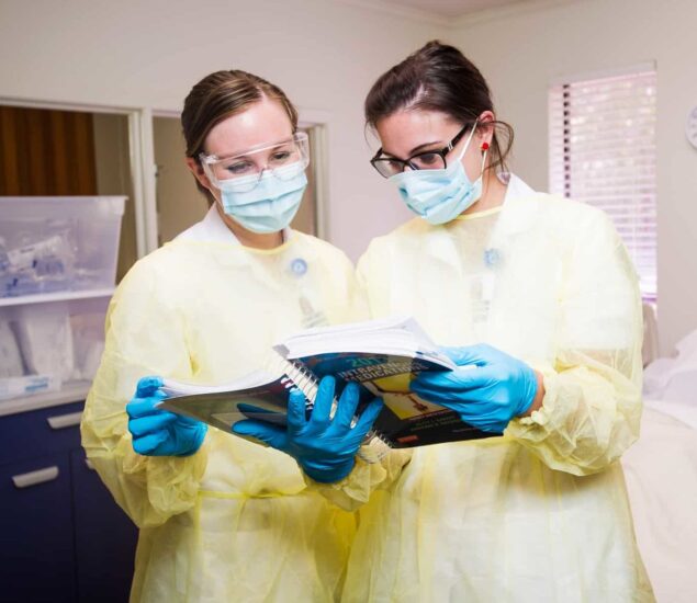 Nurses with personal protective equipment studying a book.