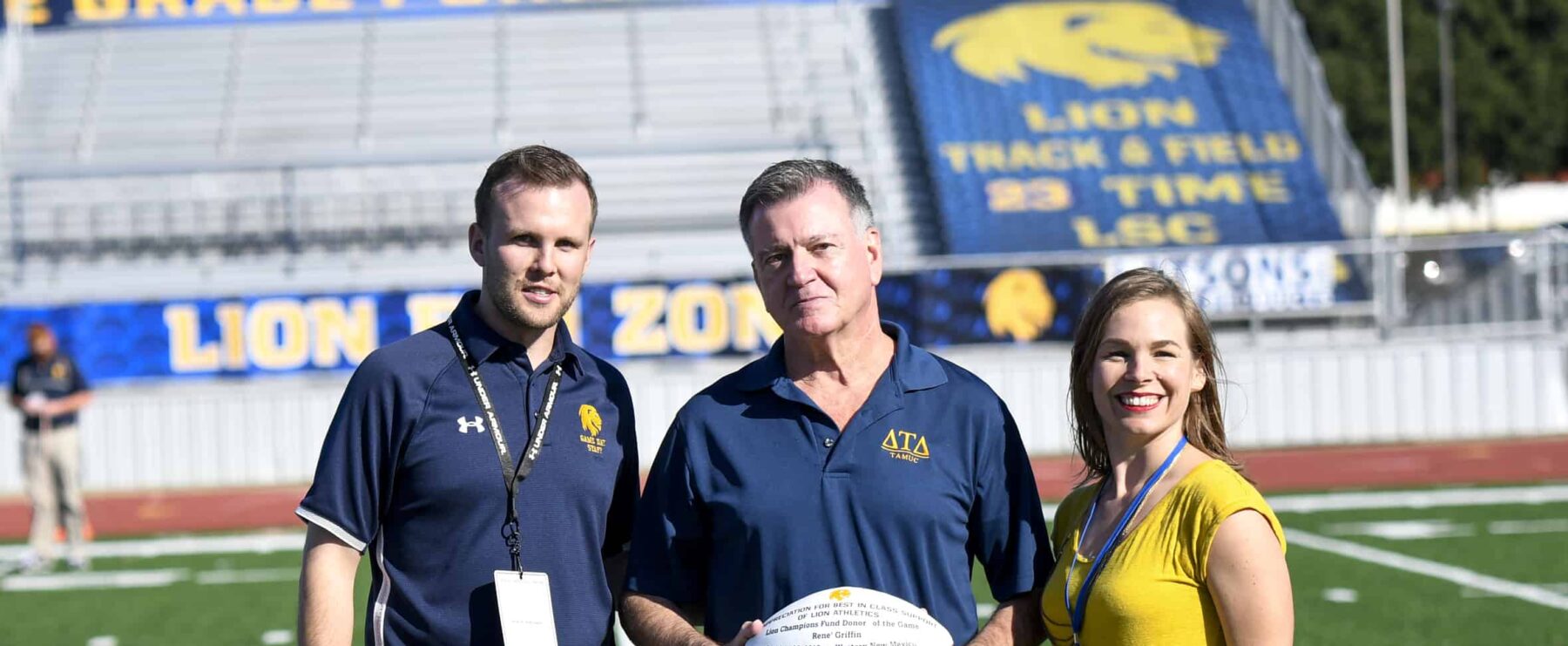 A male donor is presented with a football. He is between two other staff members from A&M-Commerce.