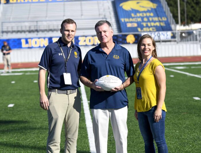 A male donor is presented with a football. He is between two other staff members from A&M-Commerce.